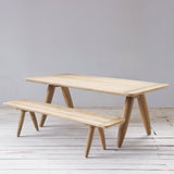 Wooden table and bench set on a light wooden floor with a plain white wall background
