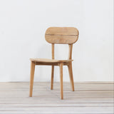 Outdoor wooden chair with rounded backrest on a wooden floor against a plain wall