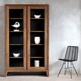 KAMA Glass Cabinet with decorative items inside and a black rattan chair next to it.