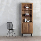 LINEA Open Bookcase with door closed next to a black rattan chair. There are white decoration items and books displayed on it.